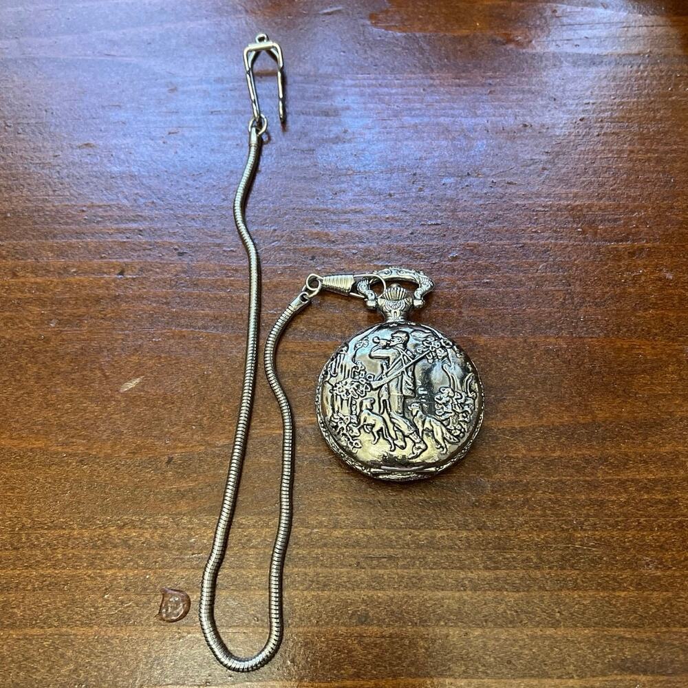 This silver-toned, embossed pocket watch features a classic "hunter and dogs"
